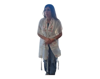 May include: A white prayer shawl with pink floral embroidery and white tassels. The shawl is draped over a person's shoulders.
