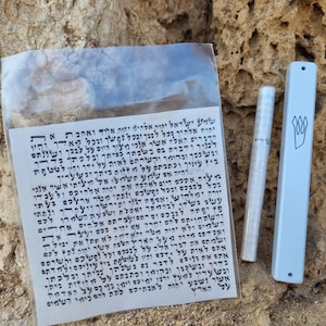 May include: A white plastic bag containing a small scroll with Hebrew text. Next to the bag are two mezuzahs, one white and one light blue. The light blue mezuzah has a black Hebrew symbol on it.