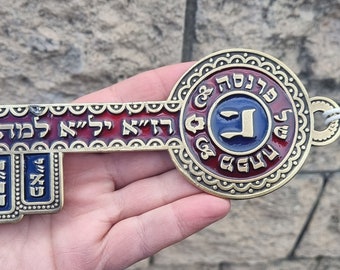 May include: A large, ornate, gold-colored key with a red and blue enamel design. The key has Hebrew writing on it, including the word "Jerusalem".