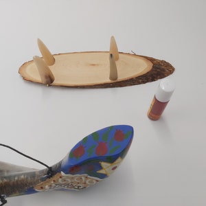 May include: A wooden base with four horn-like protrusions, a blue and white painted shofar with red flowers, and a small bottle of oil.