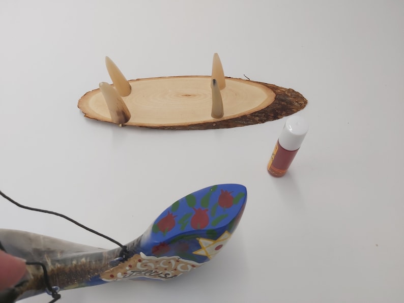 May include: A wooden base with four horn-like protrusions, a blue and white painted shofar with red flowers, and a small bottle of oil.