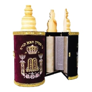 Puede incluir: Un estuche de rollo de la Torá de terciopelo burdeos con ribetes dorados y detalles bordados, incluyendo una corona, una menorá y los Diez Mandamientos. El estuche está abierto, revelando un rollo en su interior.