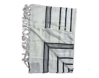 Op de afbeelding: Witte gebedssjaal met zwarte en grijze strepen en decoratieve kwastjes. De sjaal heeft een rechthoekige vorm en is opgevouwen. De hoeken hebben geborduurde vierkante ontwerpen. De stof lijkt licht van gewicht.