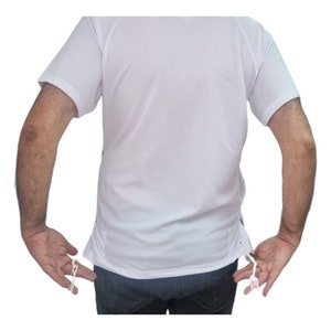 Peut inclure: Un t-shirt blanc à manches courtes avec un cordon de serrage au bas. Le cordon est blanc et a deux glands.