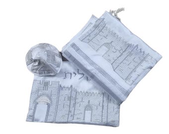 Puede incluir: Un conjunto de talit blanco con un diseño bordado en plata de un edificio con un arco y la palabra hebrea "Yerushalayim" (Jerusalén).