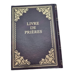 Puede incluir: Un libro encuadernado en cuero marrón oscuro con detalles dorados y el título "LIVRE DE PRIÈRES" en la portada.