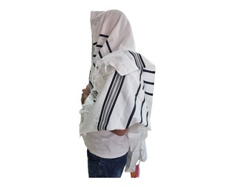 Op de afbeelding: Een witte gebedssjaal met zwarte en grijze strepen. De sjaal wordt gedragen over een wit shirt en een blauwe jeans.