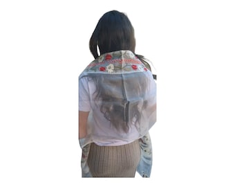 May include: A sheer white scarf with red and white floral embroidery. The scarf is draped over the shoulders of a person with long dark hair.