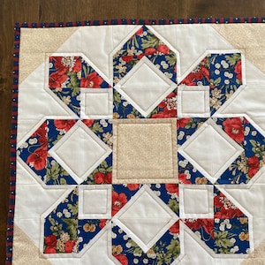 May include: A white and blue patchwork quilt with a floral pattern. The quilt is made up of squares and diamonds, and the edges are trimmed with a red and blue border.