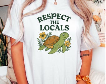 May include: White t-shirt with the text "Respect the Locals" in green. The shirt features a cartoon turtle with a brown shell and green body, surrounded by yellow flowers and green leaves.