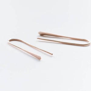 May include: A pair of simple, minimalist earrings made of rose gold metal. The earrings are thin and have a slightly curved shape.