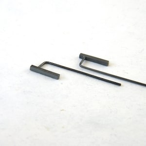May include: A pair of minimalist earrings with a thin, straight bar and a small, rectangular pendant. The earrings are made of a dark gray metal.