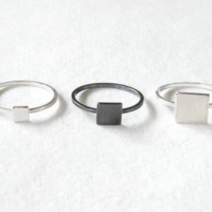 Op de afbeelding: Drie zilveren ringen met vierkante accenten. De ringen zijn in verschillende afwerkingen: gepolijst zilver, geoxideerd zilver en geblackt zilver.