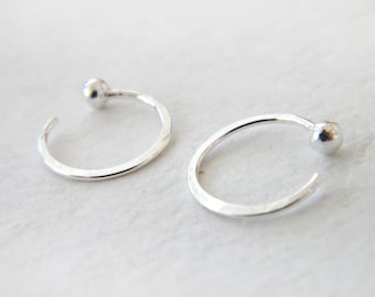 May include: A pair of silver hoop earrings with a small ball at the end of each hoop.