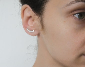May include: A silver curved bar earring worn in the upper ear cartilage.