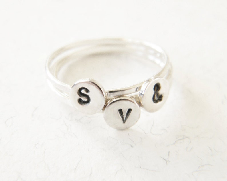 May include: A silver ring with three small charms, each with a letter stamped on it. The charms spell out "S & V".