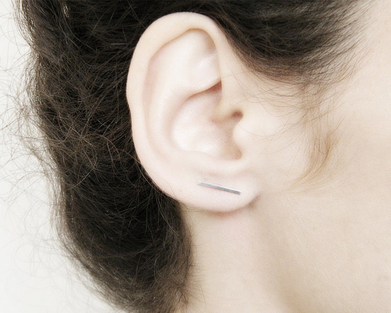 May include: A close-up of a person's ear with a thin silver bar earring.