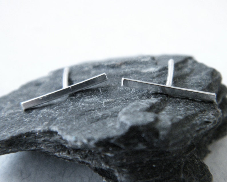 May include: A pair of silver bar stud earrings. The earrings are simple and minimalist, with a straight bar design.