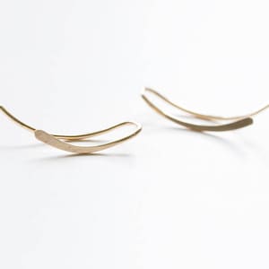 Op de afbeelding: Een paar gouden oorclips, elk met een gebogen, platte vorm. De oorclips zijn simpel en minimalistisch in design.