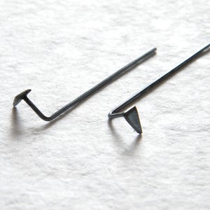 Pode incluir: Dois brincos de metal prateado com um design simples. Um brinco é uma linha reta com um pequeno triângulo na ponta. O outro brinco é uma linha curva com um pequeno triângulo na ponta.