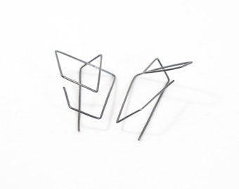 May include: A pair of dark gray metal earrings constructed from thin, bent wire forming open, angular geometric shapes. Each earring features a series of interconnected lines that create a multi-dimensional, abstract frame with sharp corners.