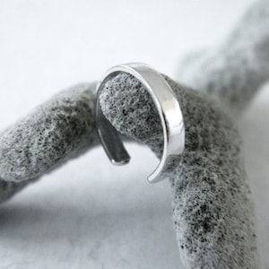 May include: A silver ring with a simple, rounded design. The ring is made of metal and has a smooth, polished finish.