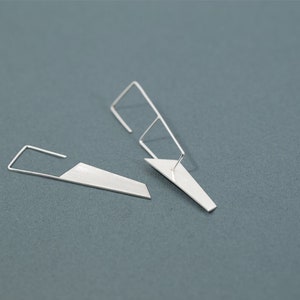 Könnte beinhalten: Ein Paar geometrische Ohrringe aus Silber mit einem scharfen, kantigen Design. Die Ohrringe sind aus dünnem Metall gefertigt und haben eine minimalistische Ästhetik.