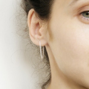 Peut inclure: Une paire de boucles d'oreilles créoles en argent avec un design fin et délicat. Les boucles d'oreilles sont présentées en gros plan, l'accent étant mis sur les boucles d'oreilles elles-mêmes.