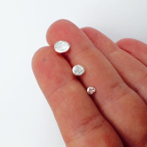 May include: Three small, hammered silver stud earrings of varying sizes. The earrings have a textured, slightly irregular surface, reflecting light. The smallest earring is approx. 0.6 cm in diameter, the medium one is 0.9 cm, and the largest is 1.3 cm.