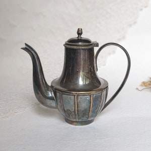 May include: A silver teapot with a fluted design and a rounded body. The teapot has a small handle and a spout.