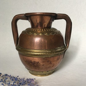 May include: A copper vase with two handles and brass accents. The vase has a round body and a flared top.