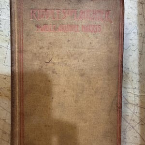 May include: A vintage book with a worn, tan cover and red lettering. The title "Riddles and Laughter" and the author's name, "Mable Annett Harris," are visible. The book has a red border and shows signs of age.