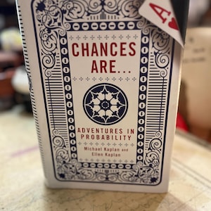 Puede incluir: Una baraja de cartas con un diseño ornamental azul y blanco. El texto "CHANCES ARE... ADVENTURES IN PROBABILITY" se muestra en rojo y blanco. Un As de Corazones asoma por la parte superior.