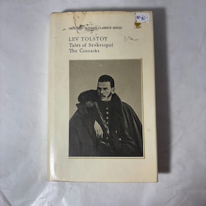 Op de afbeelding: Een vintage paperback boek getiteld "Tales of Sevastopol" en "The Cossacks" van Lev Tolstoj. De omslag toont een zwart-wit portret van een man in een donkere jas. Onderdeel van de Progress Russian Classics Series.