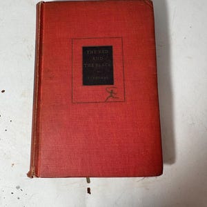 Pode incluir: Uma caneca de cerâmica branca com uma alça preta e o texto "But First, Coffee" em negrito preto. A caneca está sobre um fundo neutro, destacando seu design simples.