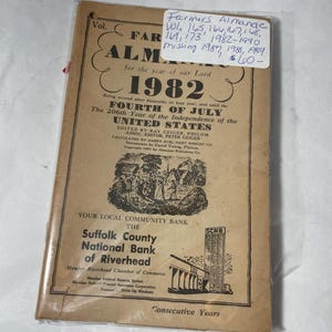 May include: A vintage 1982 Farmers' Almanac, featuring a tan cover with black text and illustrations. The cover includes the title, "Farmers' Almanac," and the year "1982." The almanac is encased in a protective plastic sleeve.