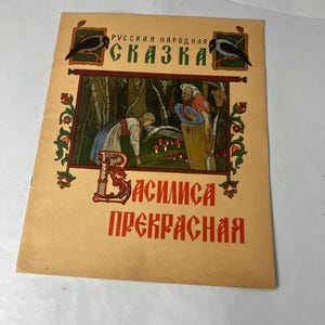 Puede incluir: Portada de libro vintage con texto e ilustraciones rusas. La portada es de color beige con detalles rojos y verdes. El título "Cuento Popular Ruso" está en la parte superior, y "Vasilisa la Hermosa" en la inferior. La ilustración muestra dos figuras en un bosque.