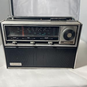 Peut inclure: Radio vintage noir et argent avec un cadran de réglage et un haut-parleur. La radio a une façade argentée, une grille de haut-parleur noire et un cadran de réglage. Le nom de la marque est visible à l'avant.