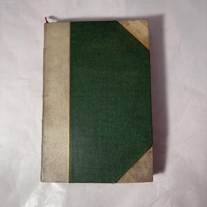 Puede incluir: Un libro antiguo con una cubierta verde texturizada y un lomo beige. Las esquinas del libro est&aacute;n reforzadas con un material de color m&aacute;s claro. Una fina l&iacute;nea dorada separa el lomo de la cubierta verde.