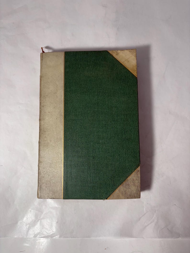 Puede incluir: Un libro antiguo con una cubierta verde texturizada y un lomo beige. Las esquinas del libro est&aacute;n reforzadas con un material de color m&aacute;s claro. Una fina l&iacute;nea dorada separa el lomo de la cubierta verde.