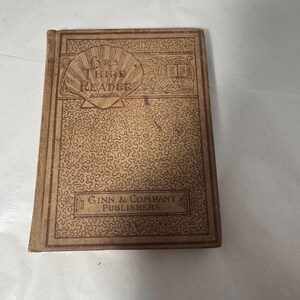 Op de afbeelding: Een vintage boek getiteld "YR'S THIRD READER" door Ginn & Company Publishers. De kaft is lichtbruin met een herhalend patroon en decoratieve elementen. De titel van het boek staat in een gestileerd lettertype en de kaft heeft een versleten uiterlijk.