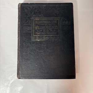 Puede incluir: Una taza de cerámica blanca con un asa negra y el texto "But First, Coffee" en negro y negrita. La taza está sobre una superficie blanca. La taza se utiliza probablemente para bebidas calientes.