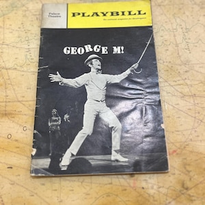 Puede incluir: Un Playbill vintage para el musical "George M!" con una imagen en blanco y negro de un hombre con traje y sombrero blancos. La portada tiene una pancarta amarilla con la palabra "PLAYBILL" y el logo del Palace Theatre.