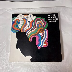 May include: A book cover featuring a black silhouette of a person's profile with colorful, swirling hair in shades of orange, blue, green, and pink. The title "MILTON GLASER GRAPHIC DESIGN" is printed in white on a black background.