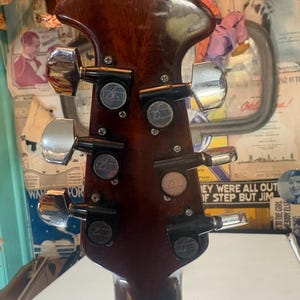 May include: Close-up of the headstock of a brown acoustic guitar. The headstock features six chrome tuning pegs and black tuning machines. The wood has a glossy finish with some wear and tear.
