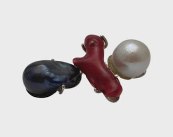 May include: A distinctive ring with a dark blue baroque pearl, a red coral piece, and a large white pearl. The ring's design combines natural elements, offering a touch of elegance and sophistication.
