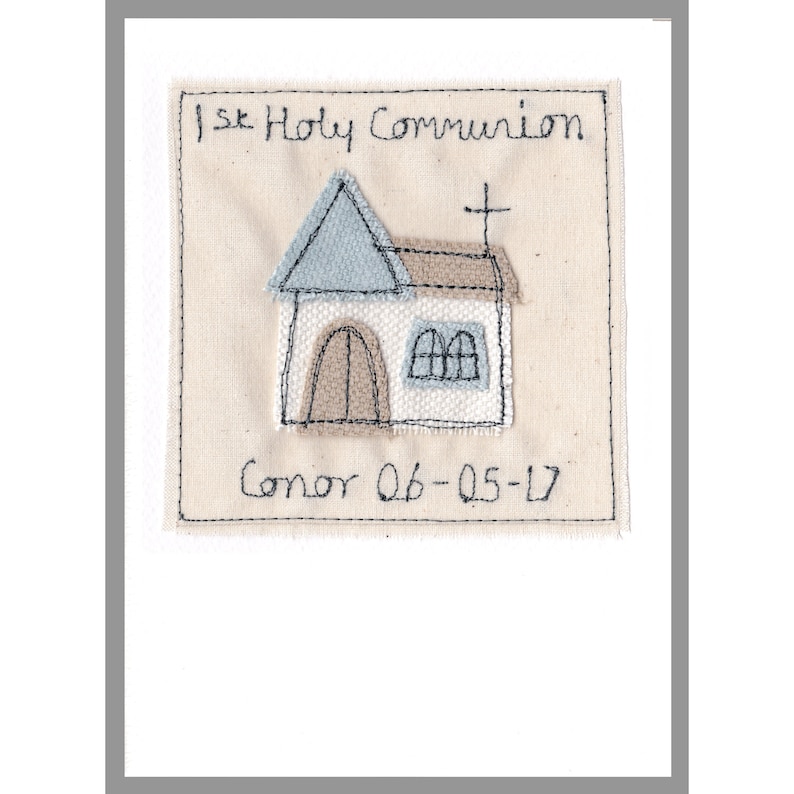 May include: A beige fabric square with a stitched image of a church building. The church has a blue roof, brown door, and two windows. The text "1st Holy Communion" is stitched above the church and "Conor 06-05-17" is stitched below.