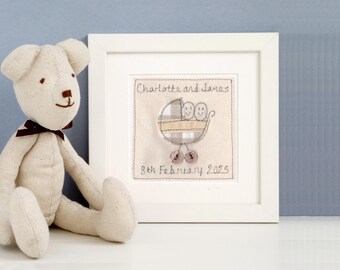 Puede incluir: Una obra de arte bordada enmarcada con un diseño de cochecito de bebé, los nombres "Charlotte and James" y la fecha "8th February 2025". Un oso de peluche con un lazo burdeos está junto al marco.