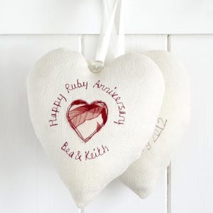 May include: Two white heart-shaped cushions with red embroidery. The larger cushion says "Happy Ruby Anniversary Bea & Keith". The smaller cushion says "40th Anniversary 2012".