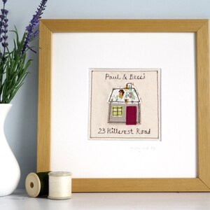 以下が含まれることがあります： 「Paul & Becci」と住所「23 Hillcrest Road」が書かれた、家の形をした刺繍が額装されています。